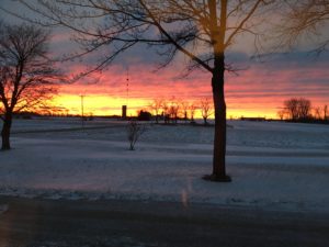 Snowy landscape with vibrant sunset and silhouetted trees.