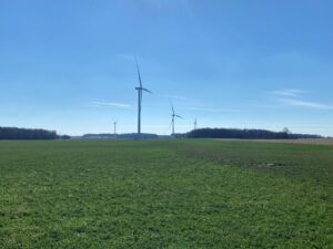 Wind turbines on a vast green field under blue sky.